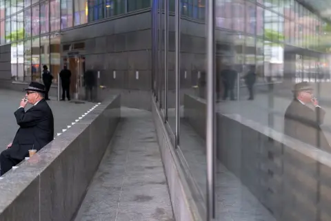Homme en chapeau fumant une cigarette, reflet dans une paroi vitrée, New York