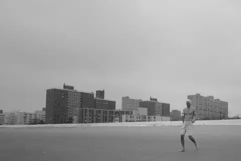 Homme souriant marchant pieds nus sur la plage, immeubles en fond, New York