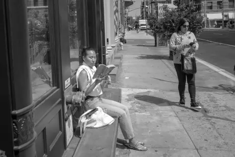 Femme lisant un livre sur un banc, passante au téléphone à proximité, New York