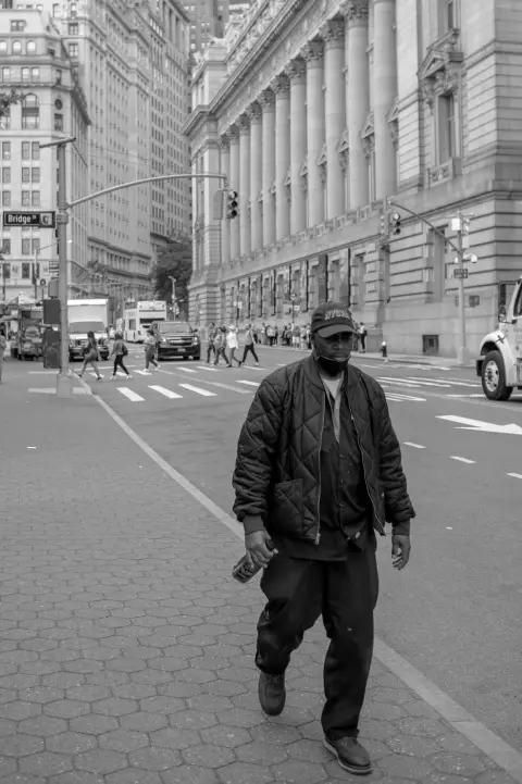 Homme masqué en blouson matelassé marchant devant les colonnes du tribunal, New York