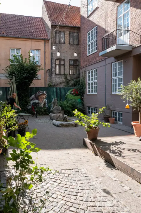 Une petite cour pavée, des plantes et une fresque au fond, Odense