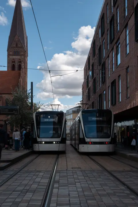Deux tramways côte à côte, une flèche d’église derrière, Odense