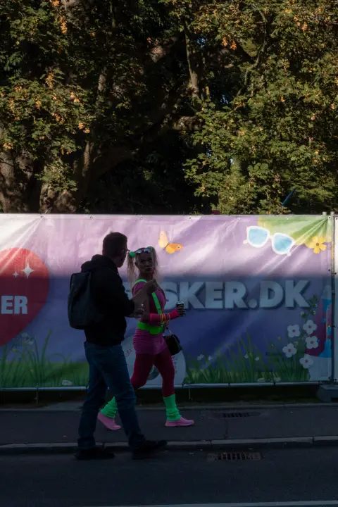 Deux passants en contre-jour devant une banderole colorée, l’une en tenue fluo, Odense