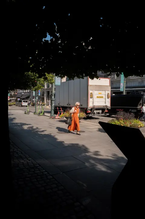 Une passante en robe orange traverse la lumière, encadrée par l’ombre d’un porche, Oslo