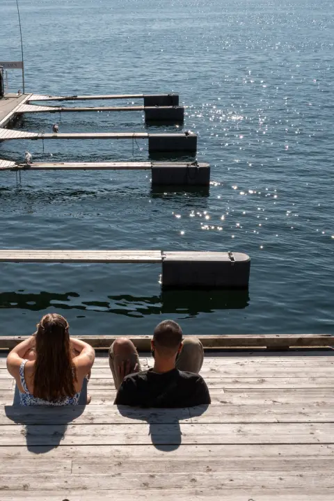 Un couple assis face à l’eau, les pontons scintillants devant eux, Oslo