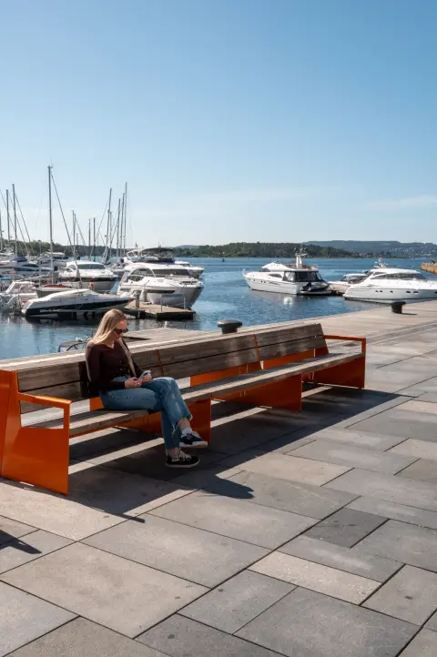Une femme sur un banc orange face aux bateaux de plaisance, Oslo