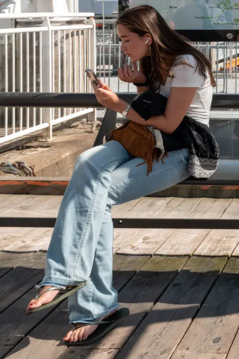Une jeune femme penchée sur son téléphone sur un banc de bois, Oslo