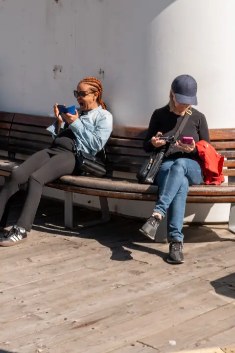 Deux femmes sur un banc, chacune sur son téléphone, Oslo