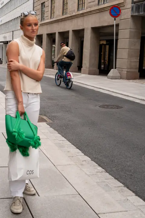 Une jeune femme au sac vert attend au bord du trottoir, Oslo