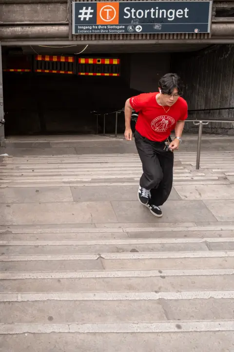 Un jeune homme en tee-shirt rouge sort en courant de la station de métro Stortinget, Oslo
