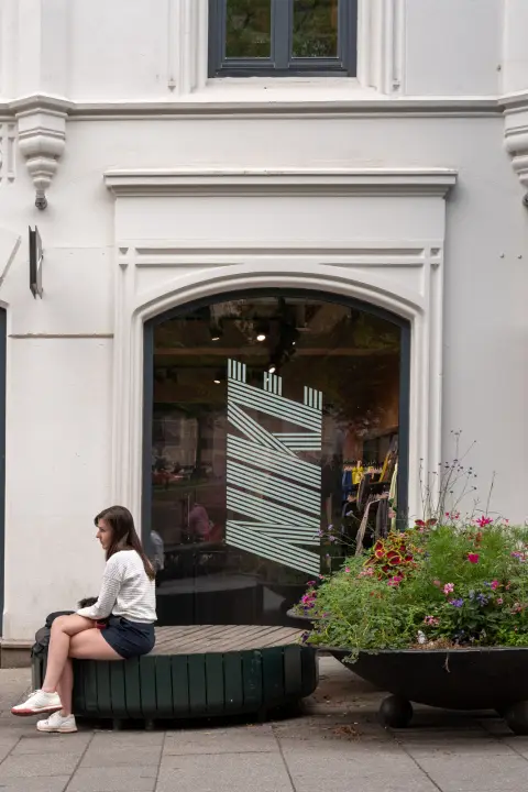 Une jeune femme assise devant la vitrine en arche d’une boutique, Oslo