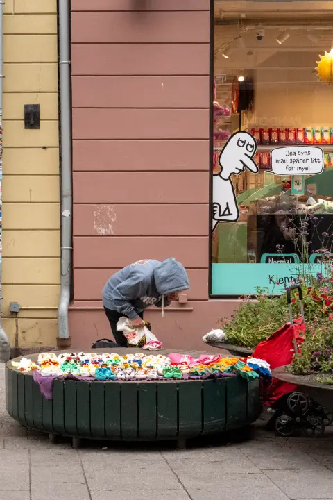 Une silhouette en capuche penchée sur une jardinière couverte d’objets colorés, Oslo