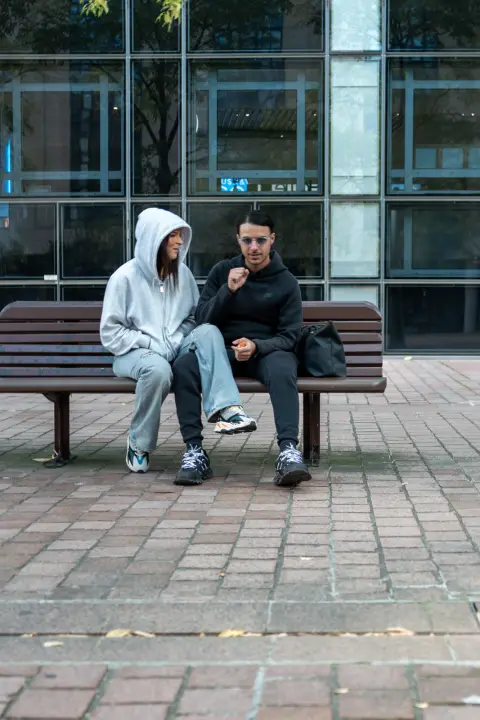 Two young people sitting on a bench in front of a glass facade, Paris
