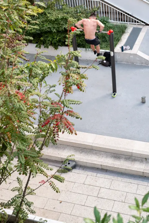 A shirtless athlete training on an outdoor bar, Paris