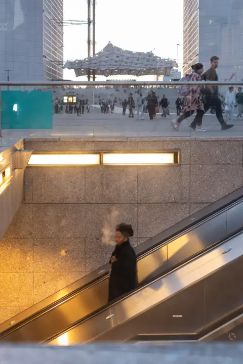 A woman blowing out smoke on an escalator, Paris