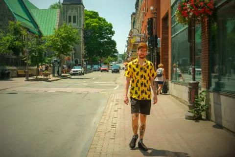 Un jeune homme en chemise jaune à motifs marche sur le trottoir, Québec