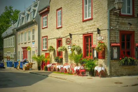 Maison de pierre aux fenêtres rouges et sa terrasse fleurie au coin d’une rue, Québec