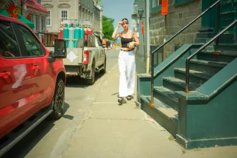Une jeune femme en pantalon blanc remonte la rue en se protégeant du soleil, Québec