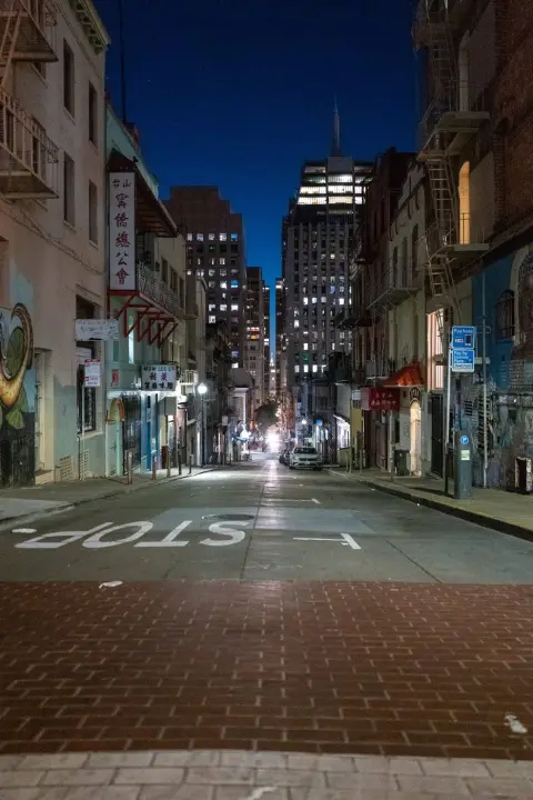Ruelle en pente de Chinatown la nuit, marquage STOP au sol et gratte-ciel au loin, San Francisco
