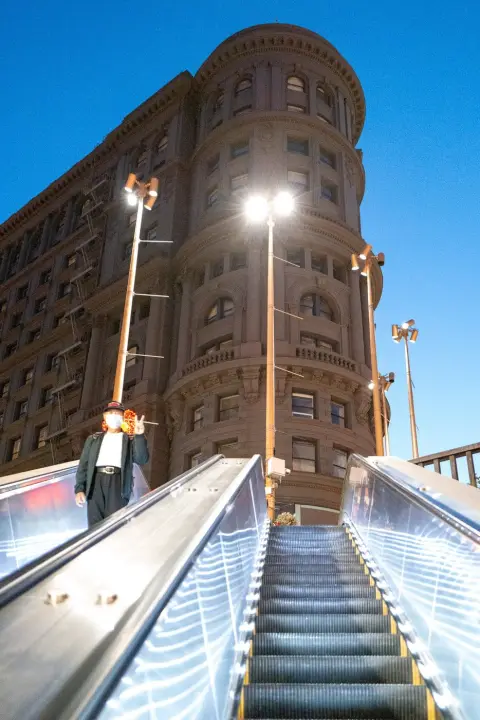 Homme faisant un signe de paix sur un escalator, immeuble d'angle classique en arrière-plan, San Francisco