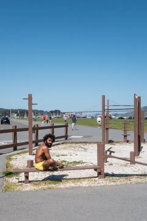 Homme torse nu assis sur un banc d'exercice en plein air, Golden Gate Bridge au loin, San Francisco