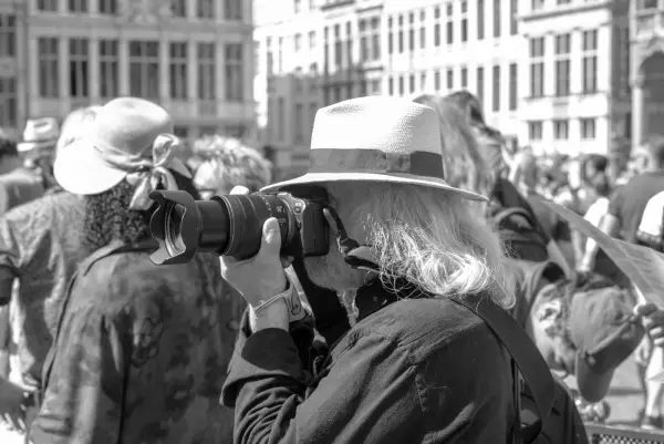 Photographe au chapeau de paille et au téléobjectif devant les façades anciennes, Zinneke Parade, Bruxelles (planche 013)