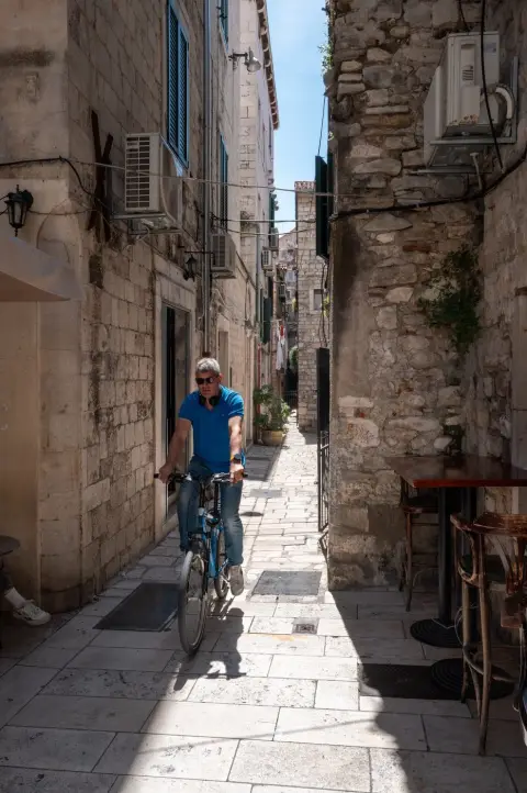 Cycliste en polo bleu traversant une ruelle etroite, Split