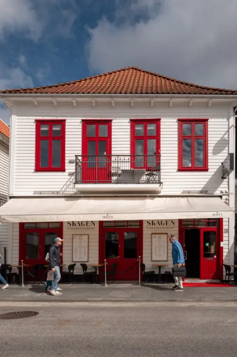 Une maison blanche aux fenêtres rouges, deux passants devant, Stavanger