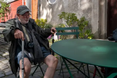 Un vieil homme à la canne et à l’appareil photo assis à une table verte, Stavanger