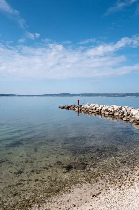 Silhouette d'un pêcheur en rouge au bout d'une pointe rocheuse, Trogir