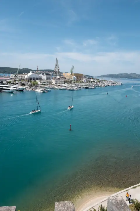 Deux voiliers de régate quittant le port sous les grues du chantier, Trogir