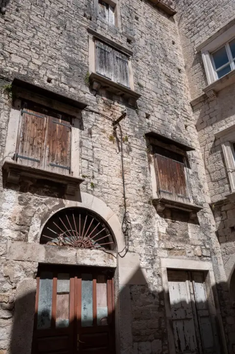Façade usée aux volets de bois et porte vitrée fatiguée, Trogir