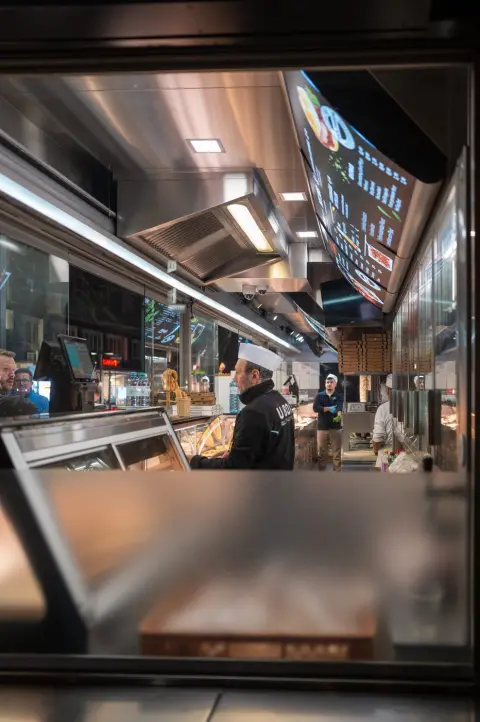 Cuisinier en toque servant sous les menus lumineux d'un snack, Vienne