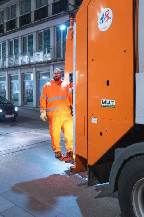 Eboueur en tenue fluo au marchepied du camion de collecte, Vienne