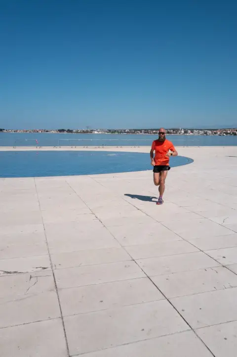 Coureur barbu en tenue orange longeant le bassin du front de mer, Zadar