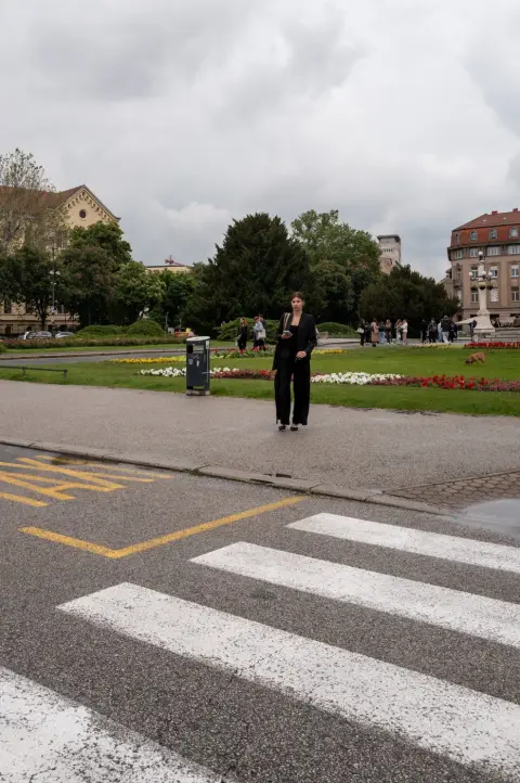 Une femme en tailleur noir traversant près d'un parc fleuri, Zagreb