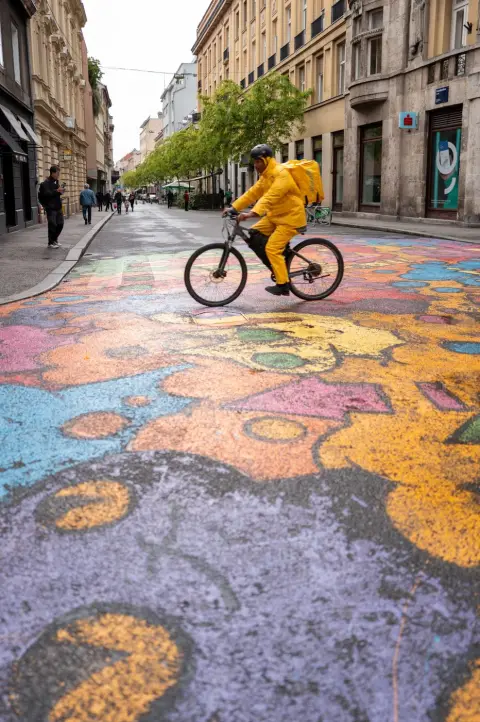 Livreur à vélo traversant une fresque colorée peinte sur la chaussée, Zagreb