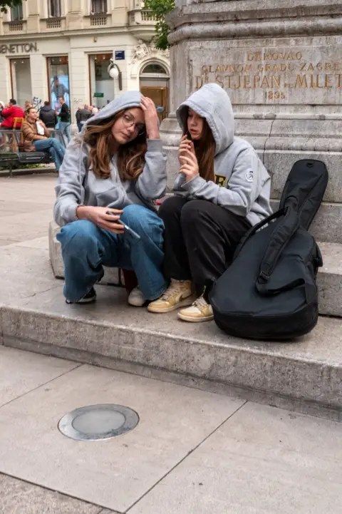 Deux adolescentes en sweat à capuche assises près d'un étui de guitare, Zagreb