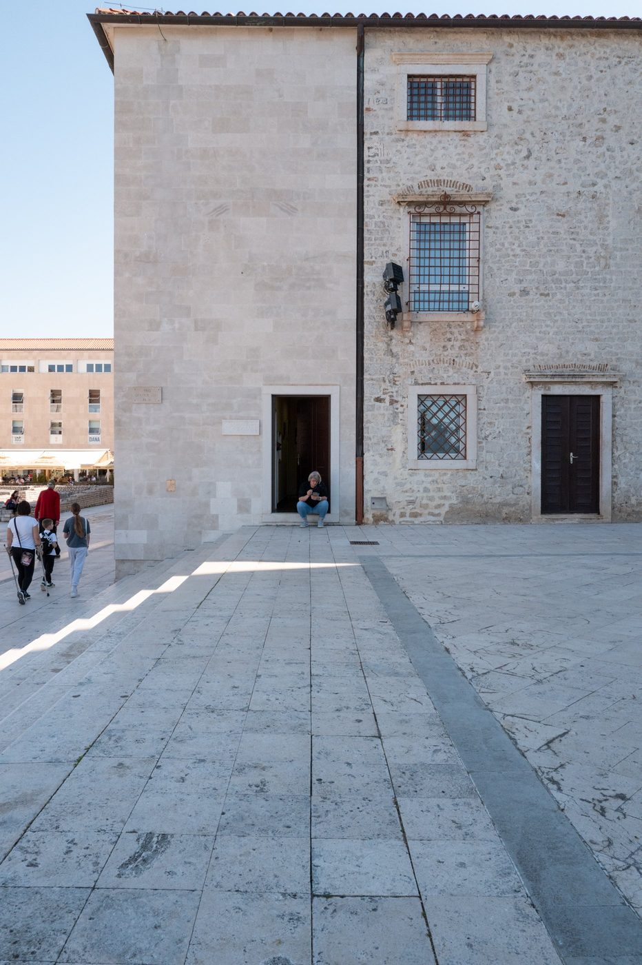 A passerby sitting in the doorway of a light stone building, Zadar