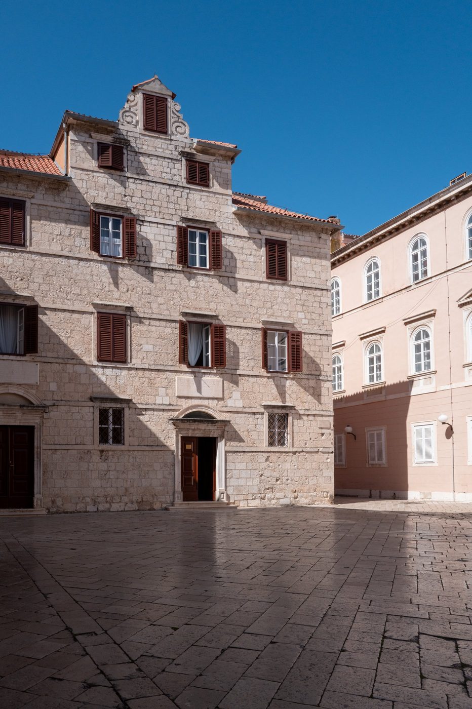 Renaissance façade with brown shutters overlooking an empty square, Zadar