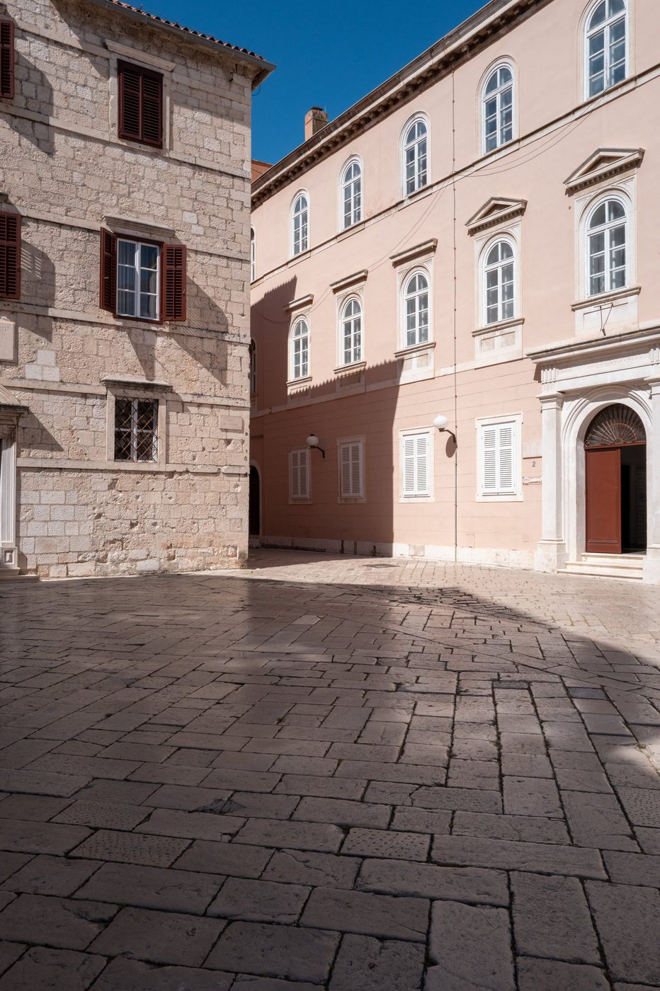 Corner between a stone façade and a pink building on a deserted square, Zadar