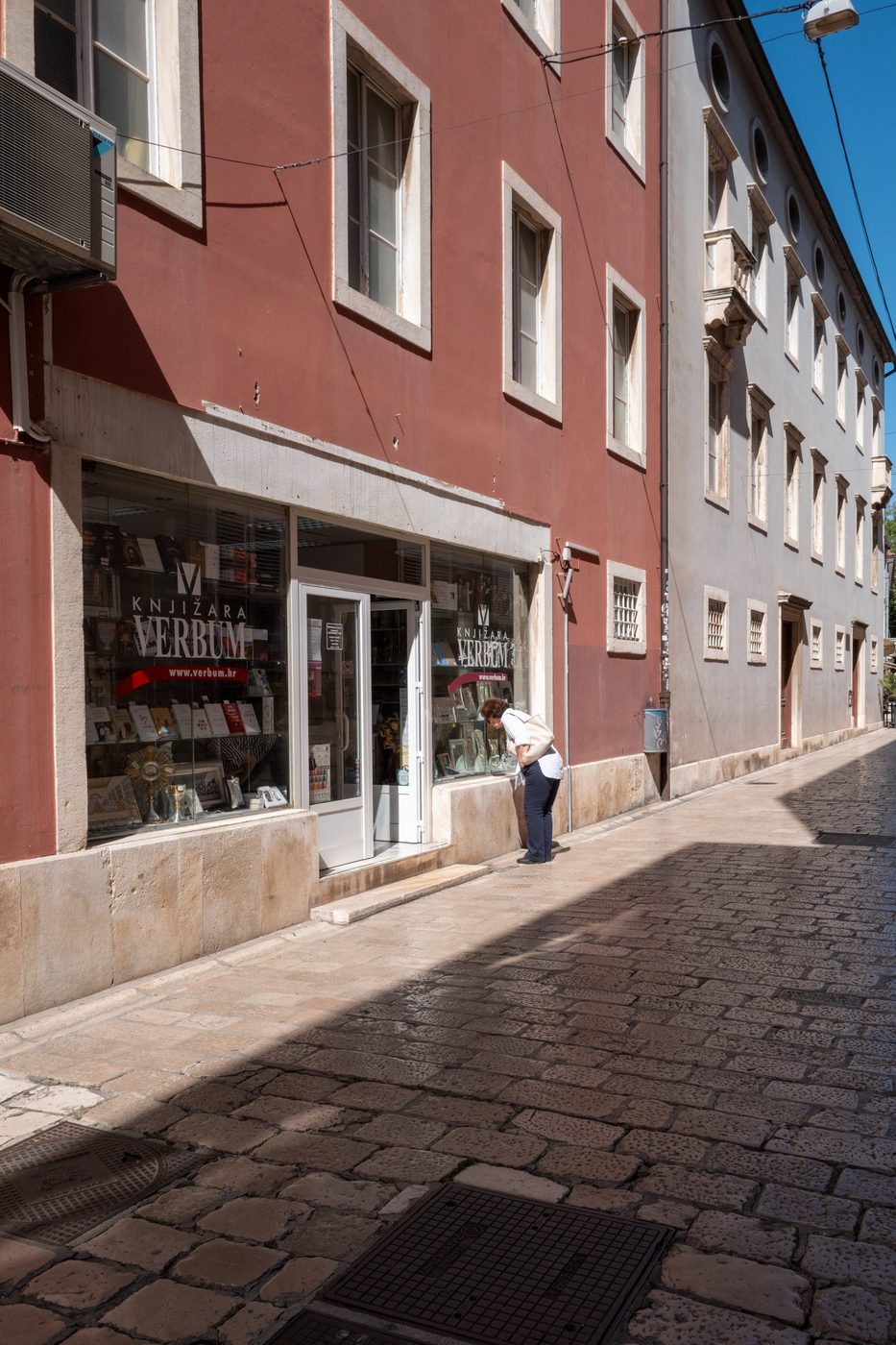 A passerby looking at the window of a bookshop with a red façade, Zadar
