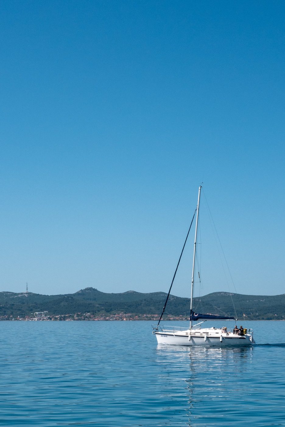 Solitary sailboat gliding on a calm sea facing the coast, Zadar