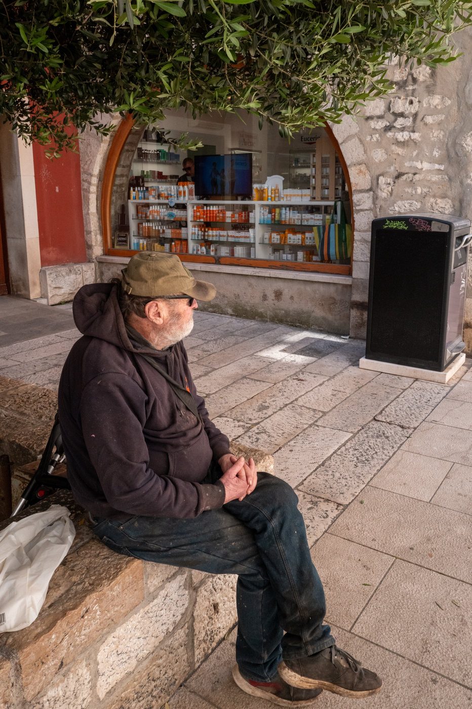 An elderly man sitting facing the window of a shaded pharmacy, Zadar