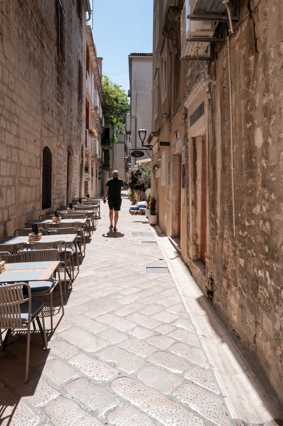 A man walking away down an alley lined with a restaurant terrace, Zadar
