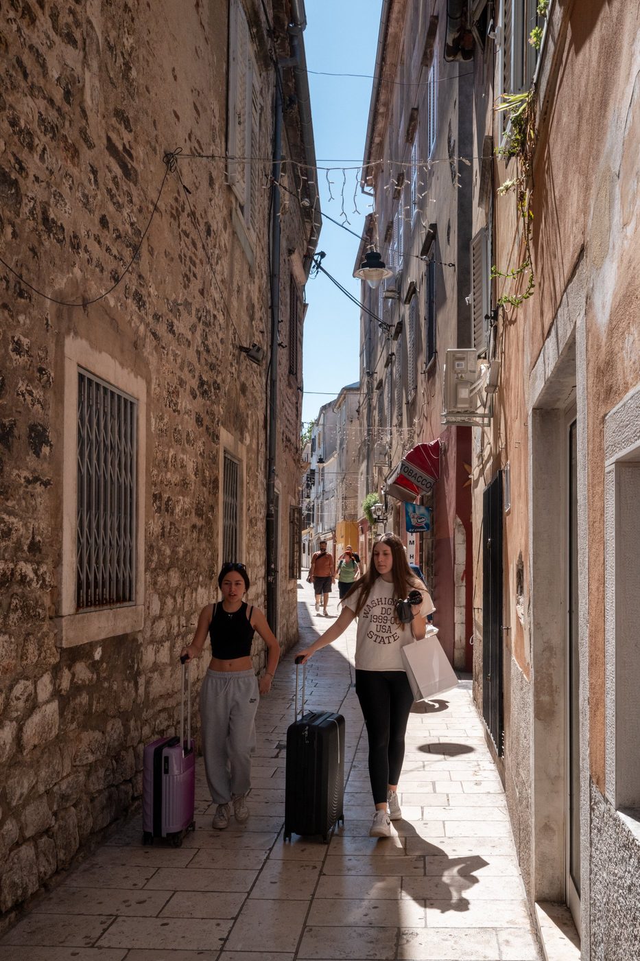 Two tourists pulling their suitcases down a busy alley, Zadar