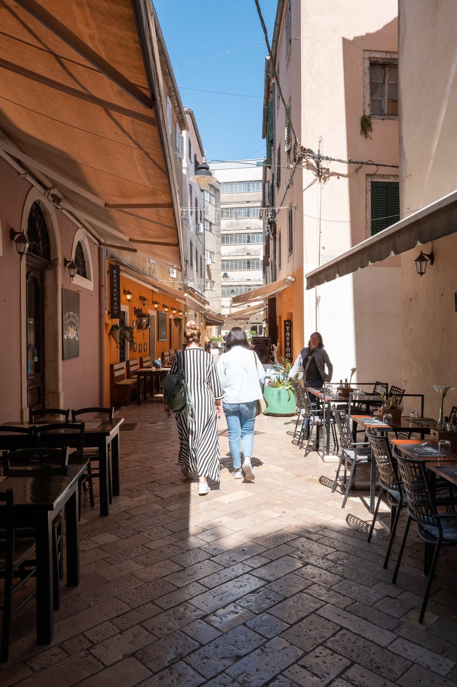 Two passersby walking beneath the orange awnings of a shopping alley, Zadar