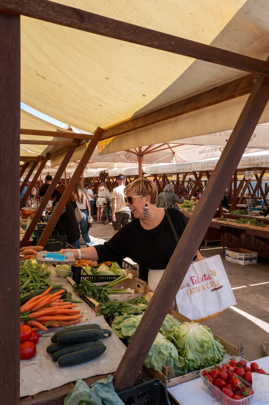 Smiling vendor surrounded by fresh vegetables beneath a yellow awning, Zadar