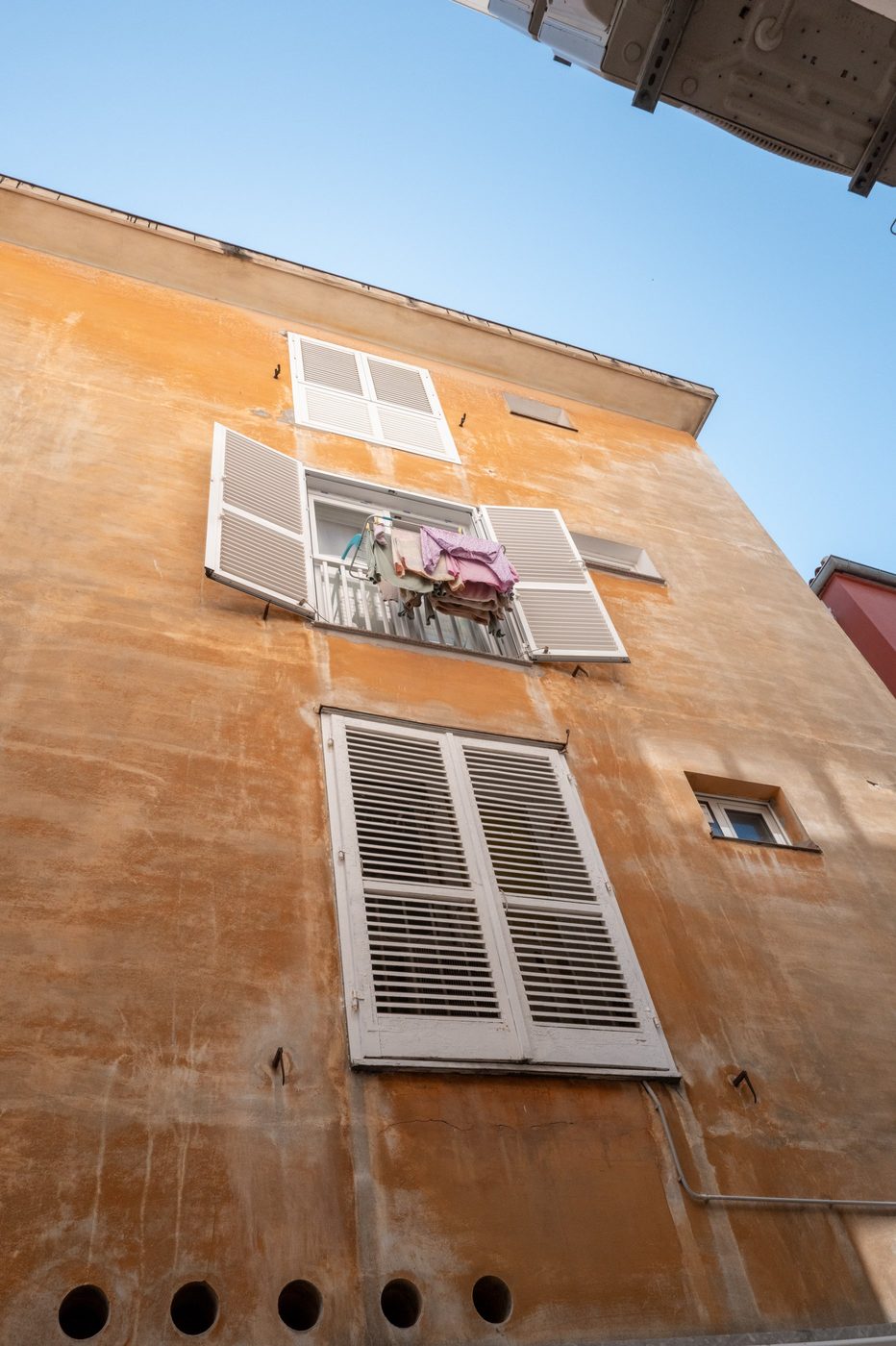 Laundry drying at the window of an ochre façade with white shutters, Zadar