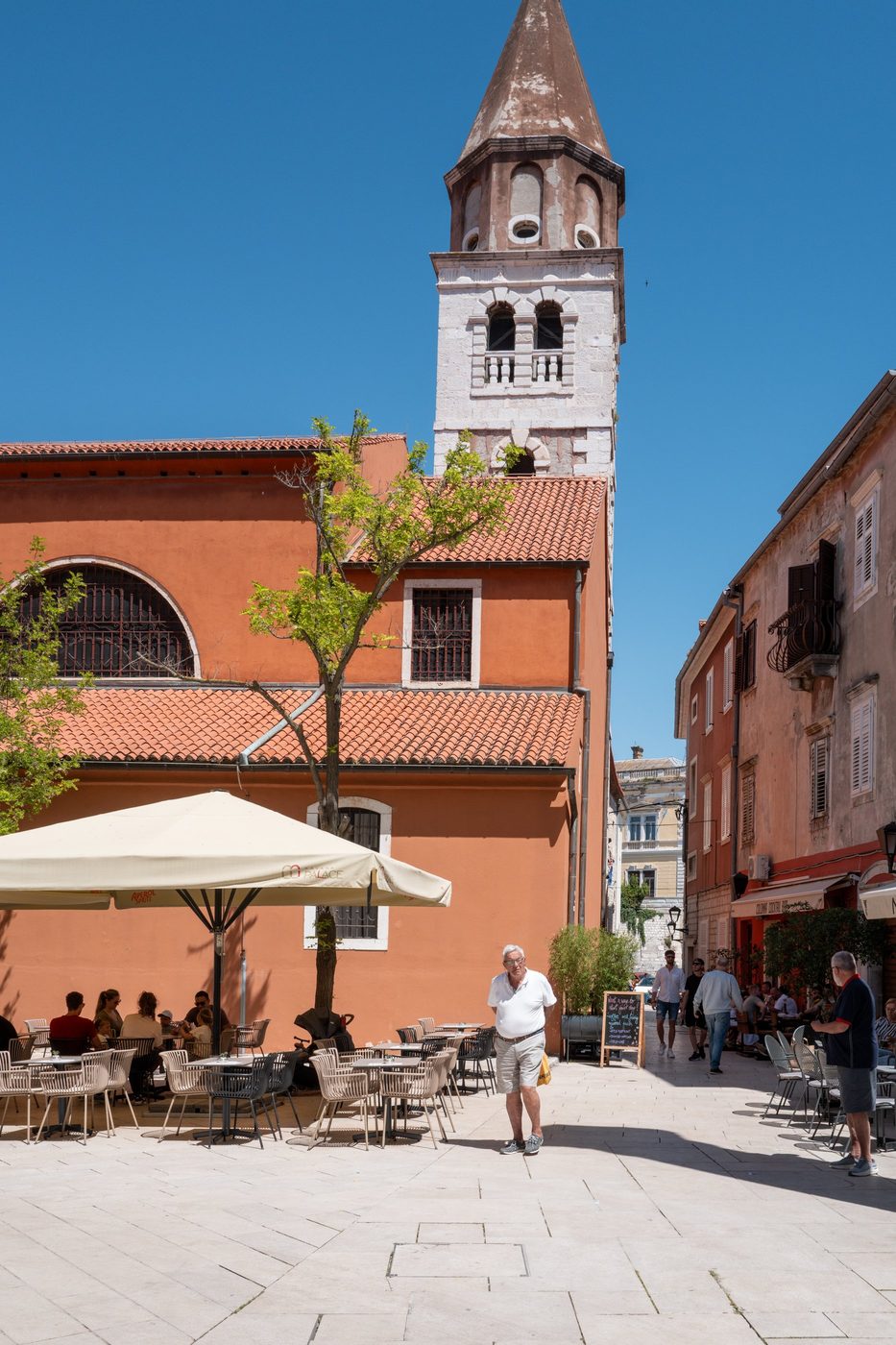 A passerby in front of the orange church and its octagonal bell tower, Zadar